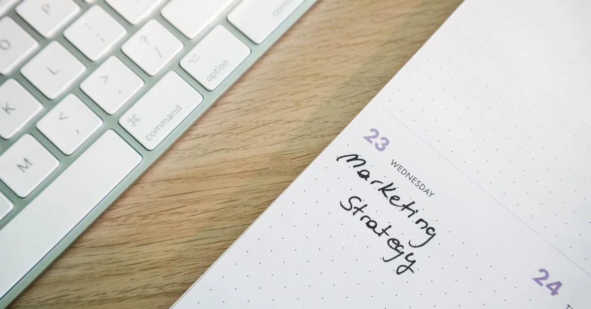 Gros plan sur un bureau avec un clavier et un calendrier ouvert sur une note de stratégie marketing.