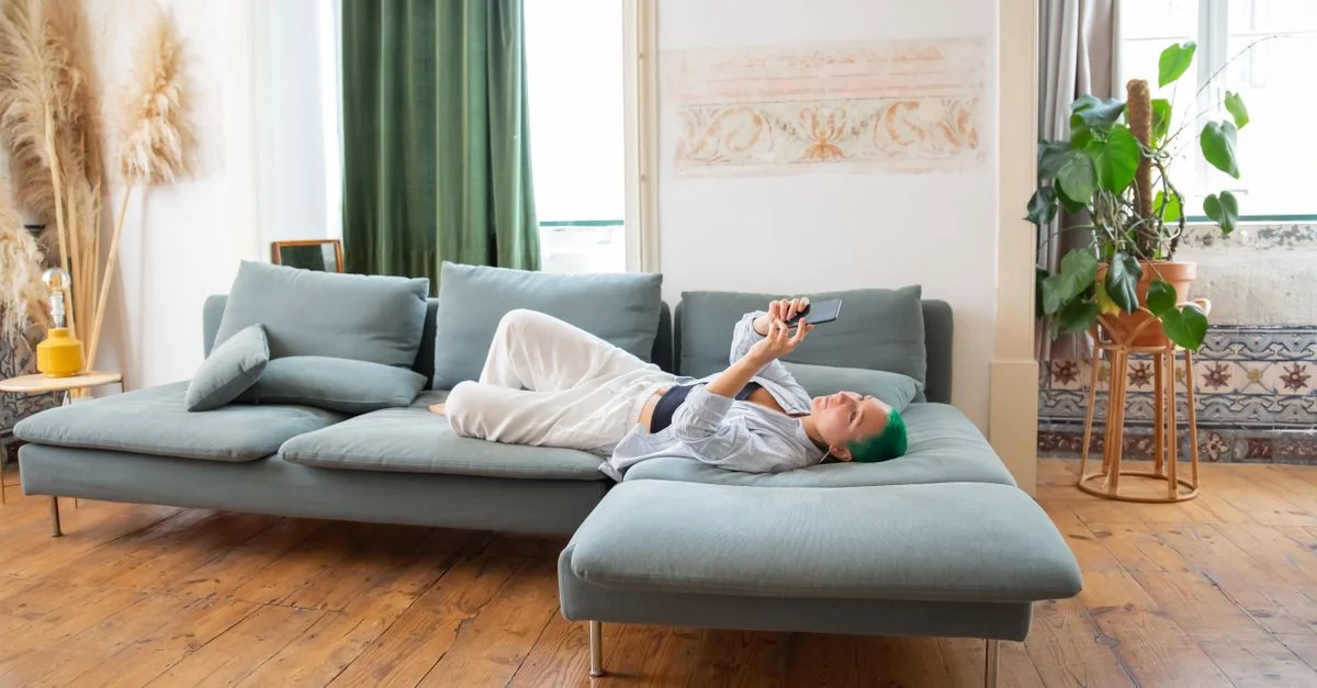 Femme aux cheveux verts se détendant sur un canapé en utilisant un smartphone à la maison