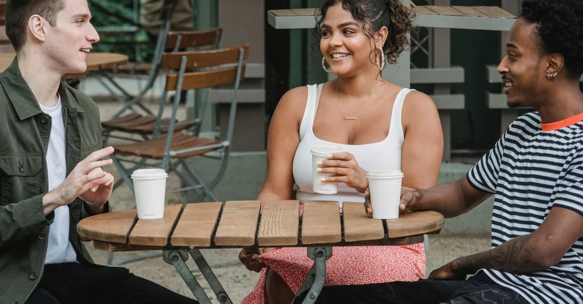 Trois amis discutent et profitent d'un café en extérieur. Atmosphère vibrante et détendue.