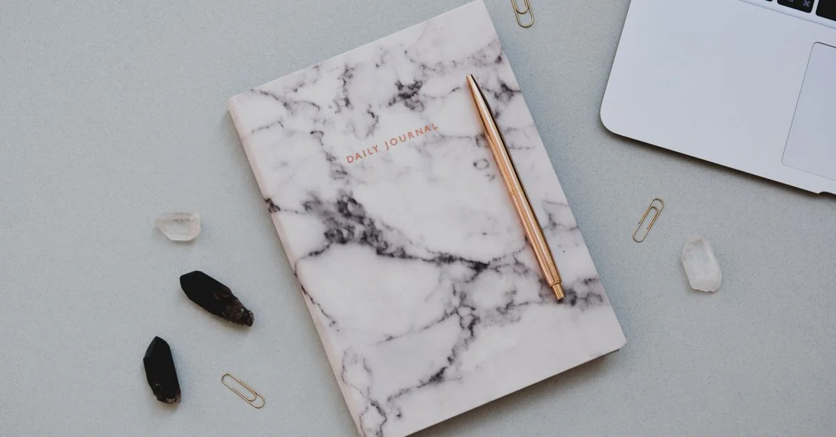 Journal en marbre avec des cristaux et un ordinateur portable en disposition élégante sur un bureau, parfait pour des espaces de travail créatifs.